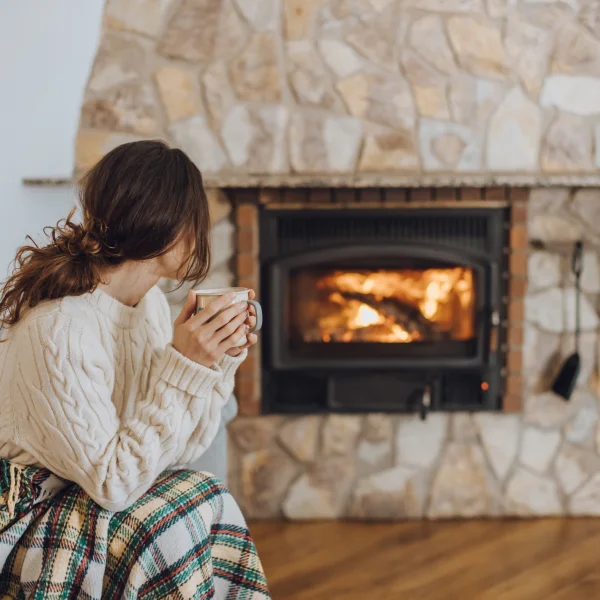 Foyer au gaz: choisir le bon foyer pour ambiance parfaite 2 Une femme assise devant un poêle, tenant une tasse de café, profitant de la chaleur et de l'ambiance chaleureuse.